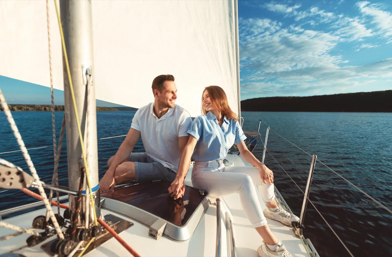 Couple holding hands on a sunlit sailboat gliding across Puget Sound with the Seattle skyline behind them