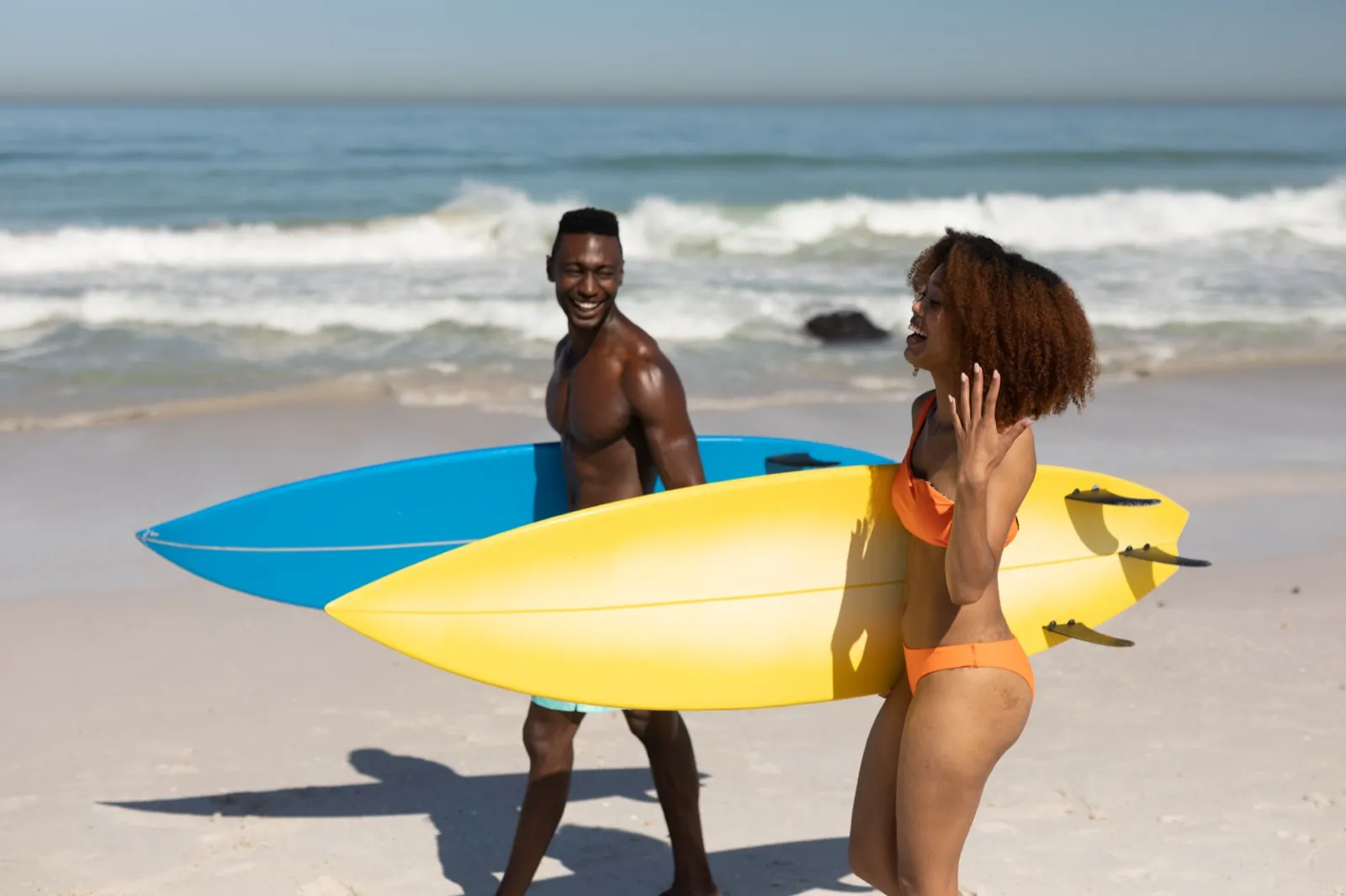 Couple holding surfboards on a Hawaiian beach ready for a surf lesson