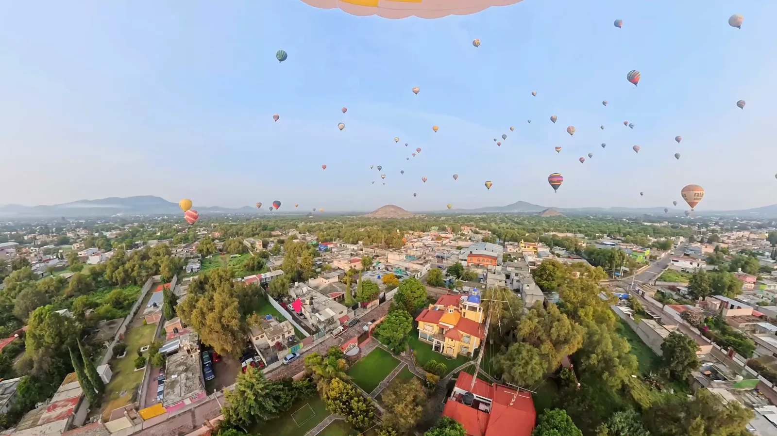 Dozens of hot air balloons in the sky at sunrise with the Pyramid of the Sun on the horizon