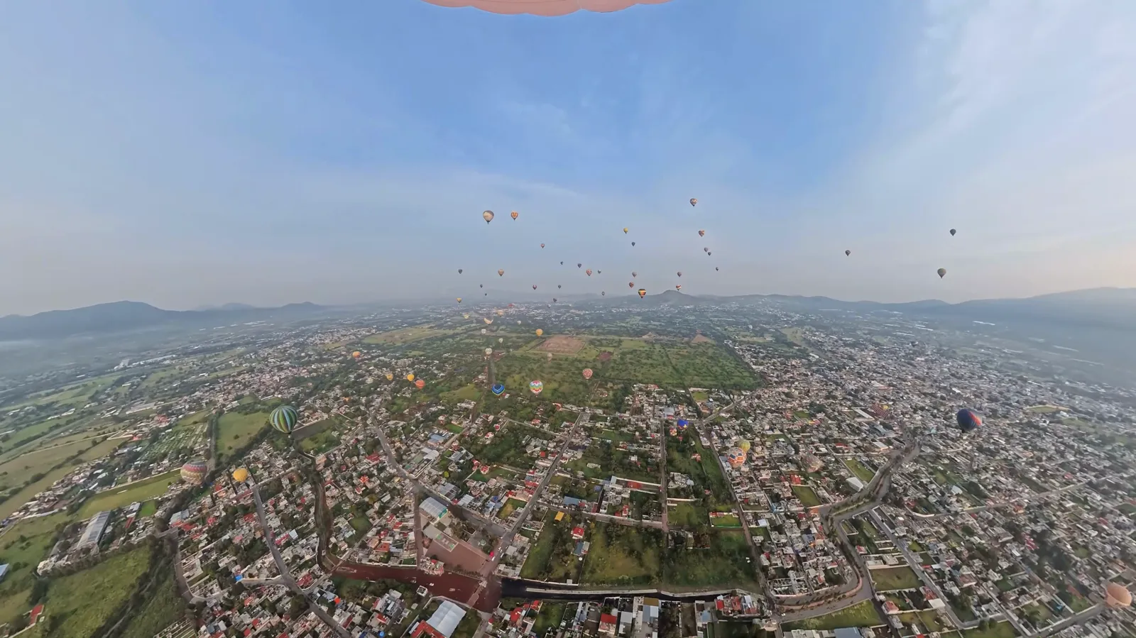 Wide view from inside a balloon basket over the valley with balloons scattered across the sky