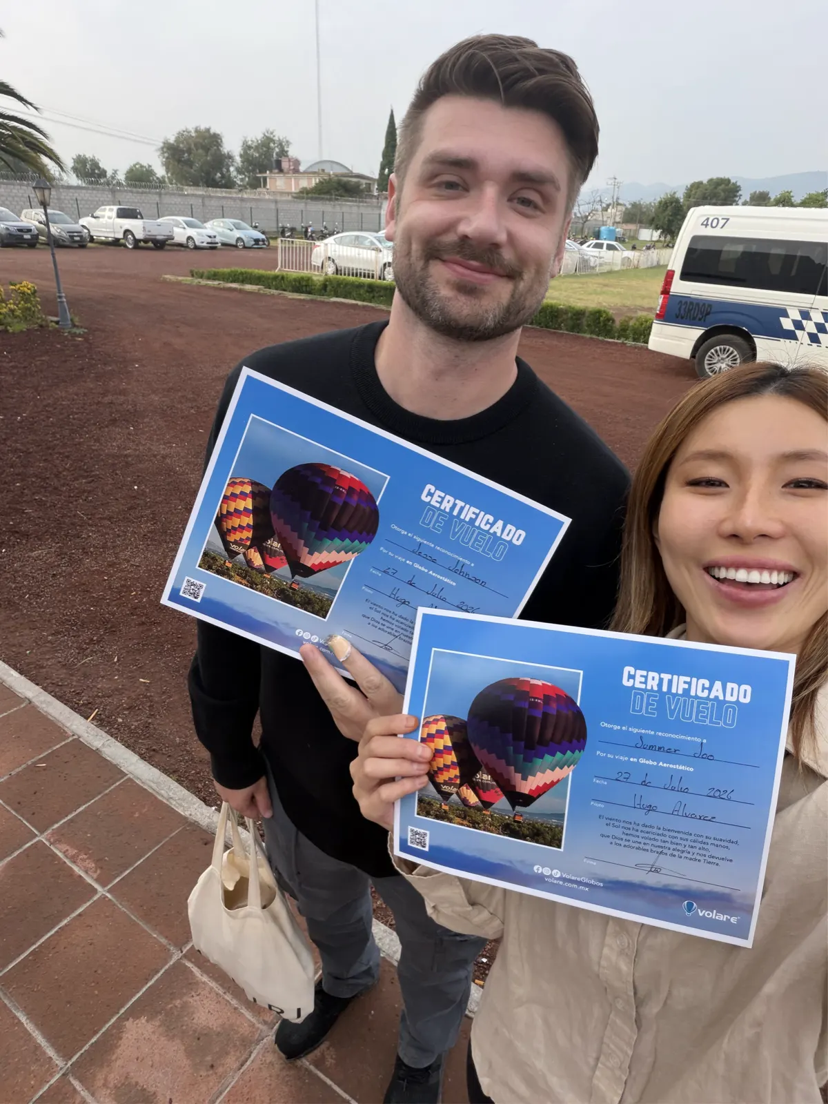 Couple holding two printed Volare flight certificates in the parking area after landing