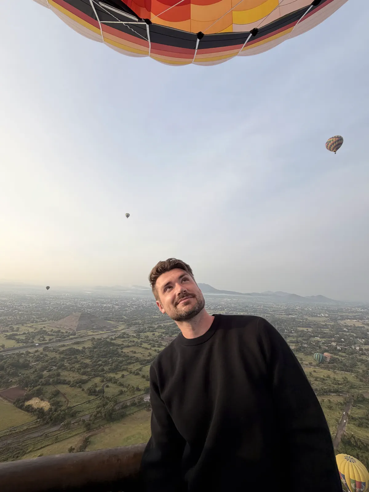 Looking up at the underside of a striped hot air balloon envelope with the Teotihuacan valley and other balloons below
