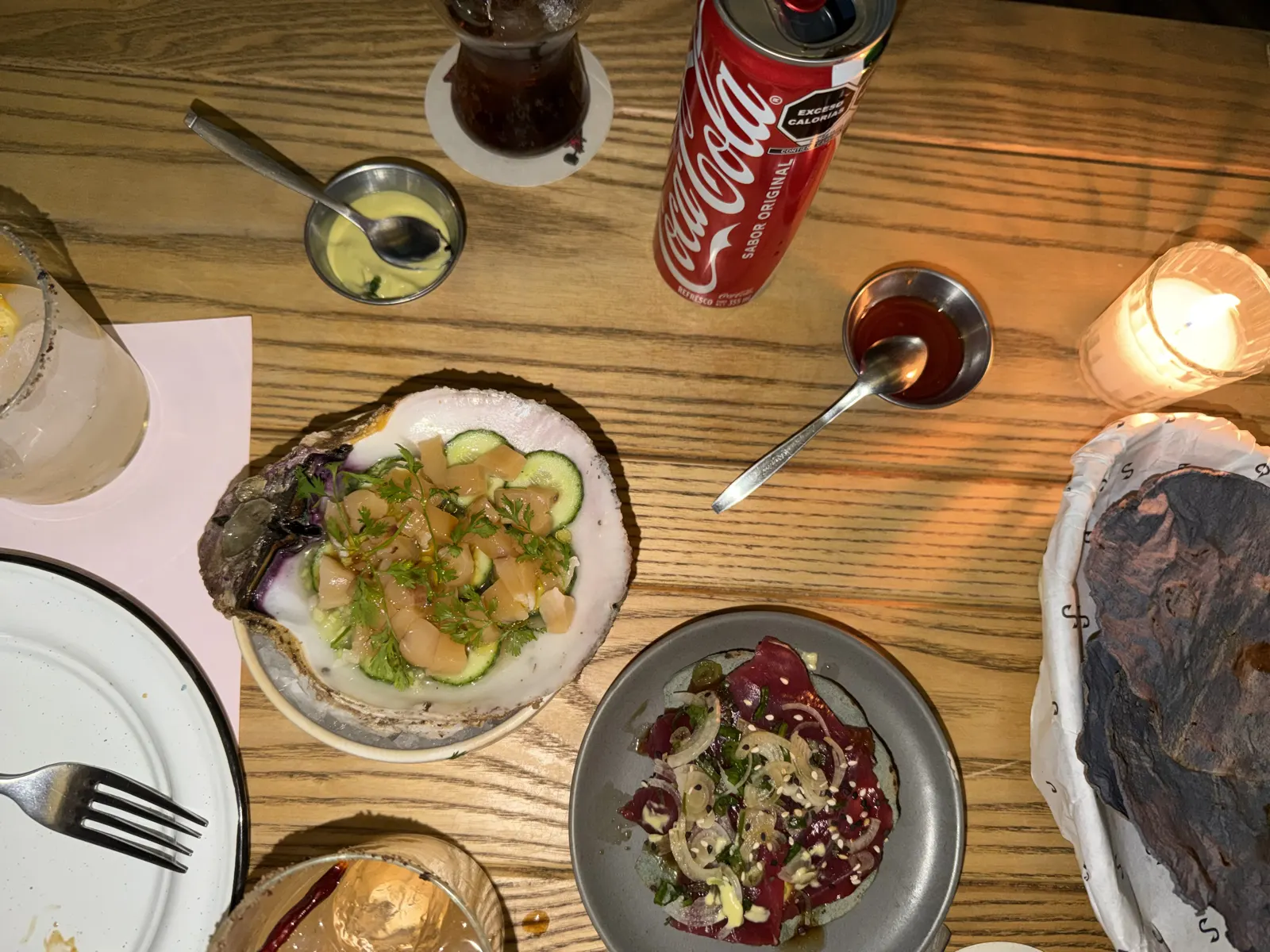 Overhead view of a table with aguachile served in a shell, beef carpaccio, tortillas, and cocktails