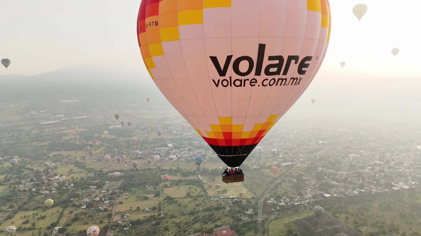 Drone view of a Volare hot air balloon over the Teotihuacan valley with other balloons below
