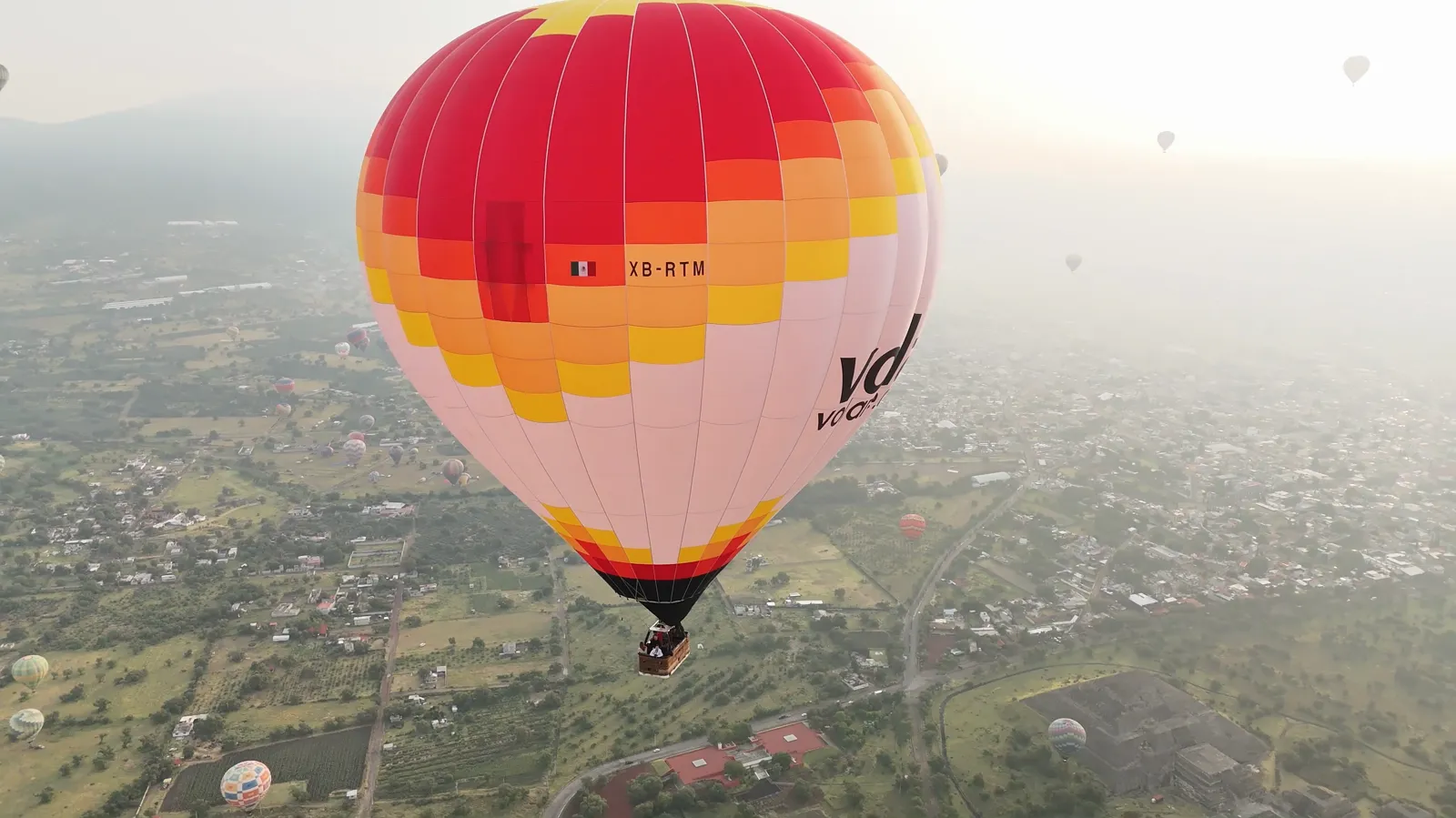 Drone view of a white and red hot air balloon high over the valley in morning haze