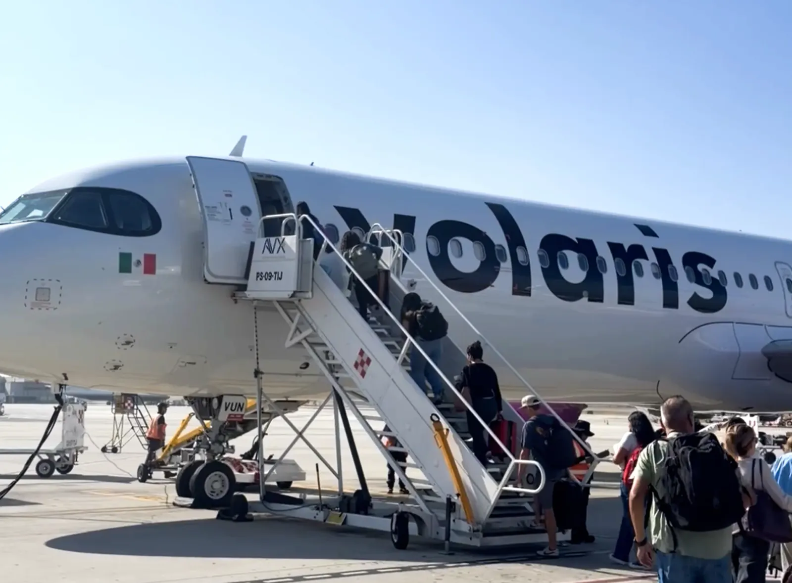 Passengers boarding a Volaris plane on the tarmac at Tijuana airport under a clear sky