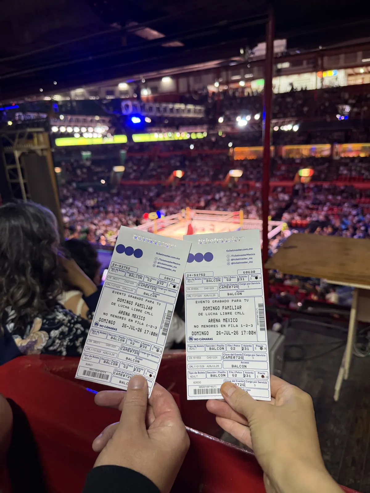 Two Arena Mexico Lucha Libre tickets held up above the packed arena and the lit ring below