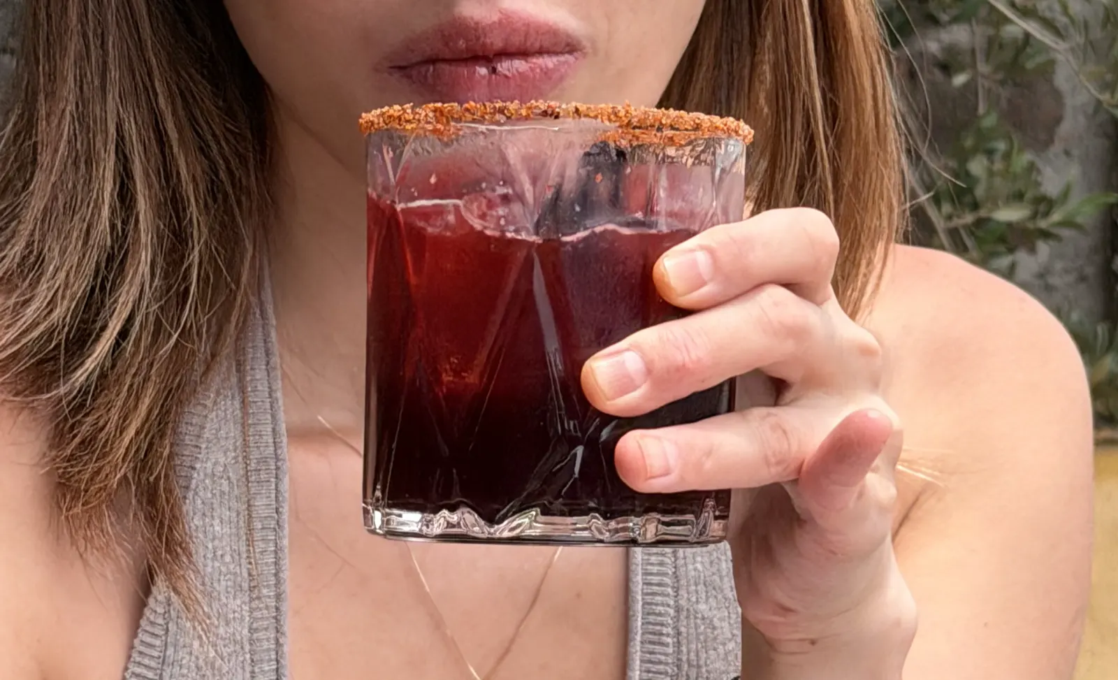 Close-up of a mezcalita cocktail with a chili-salt rim being held up outdoors