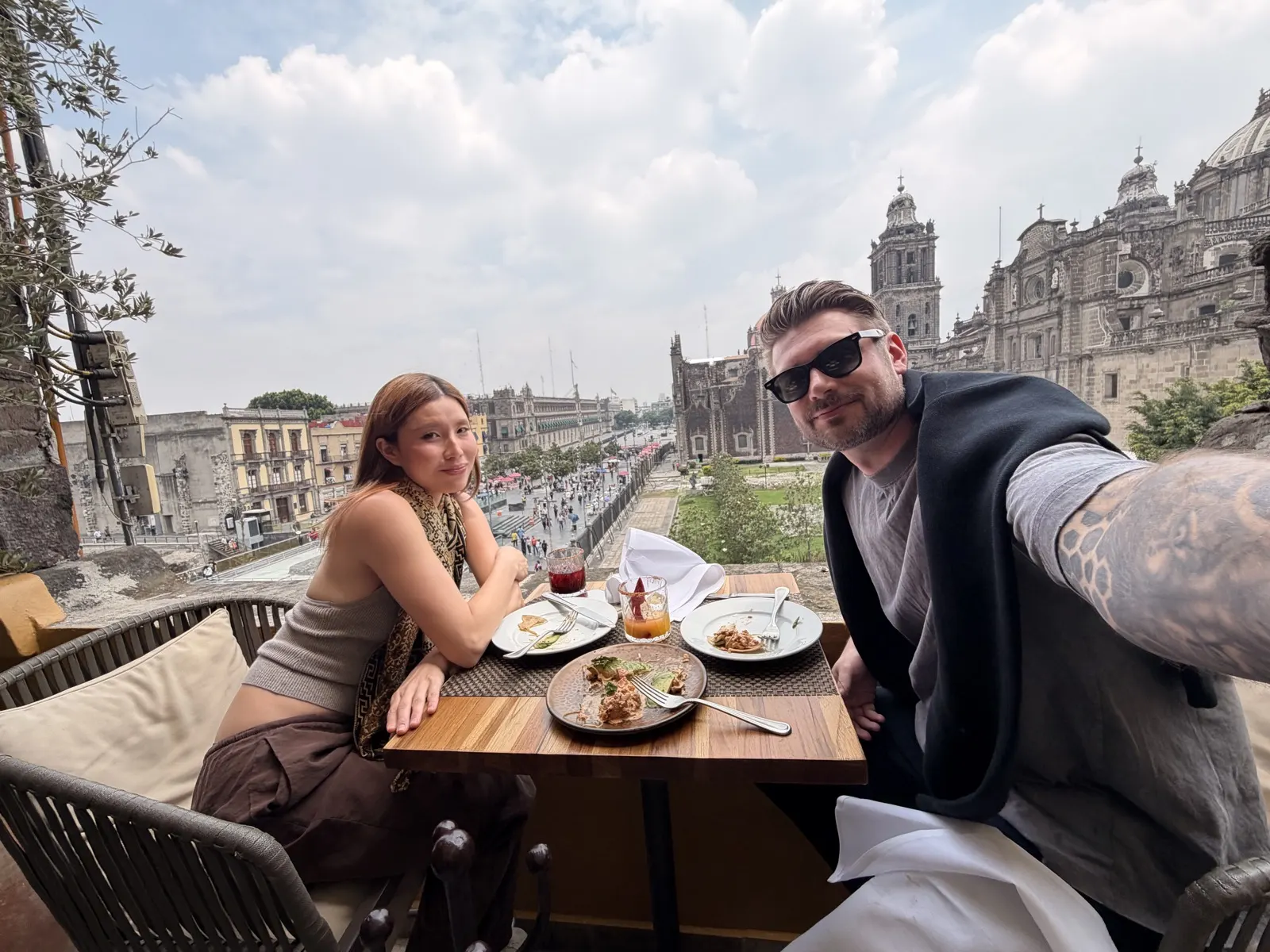 Couple at a rooftop restaurant table with mezcalitas and the Metropolitan Cathedral behind them