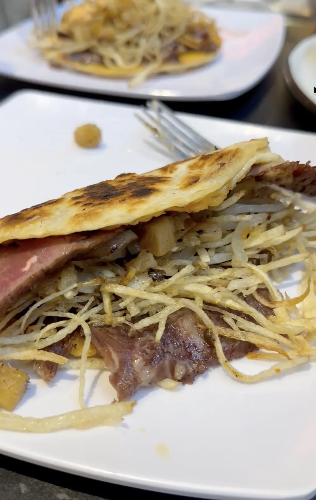 Close-up of a grilled taco stuffed with steak and shoestring potatoes on a white plate at Tosco Restaurante